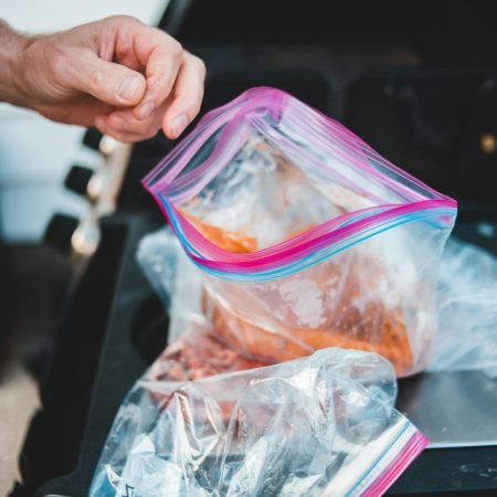 Close-up of hand preparing marinated meat in a Ziploc bag on a grill.